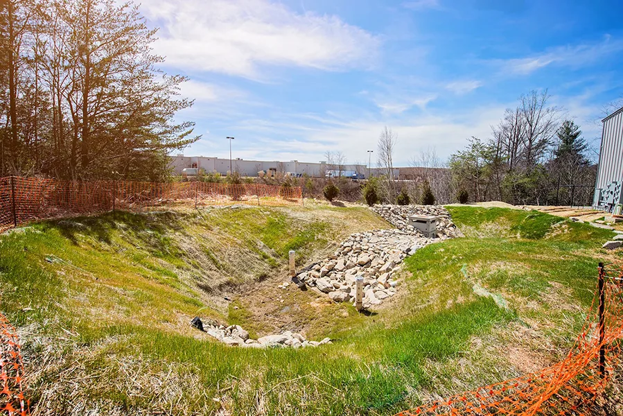 Commercial site work with a rock-lined drainage channel and erosion-control fencing in Asheville, NC.