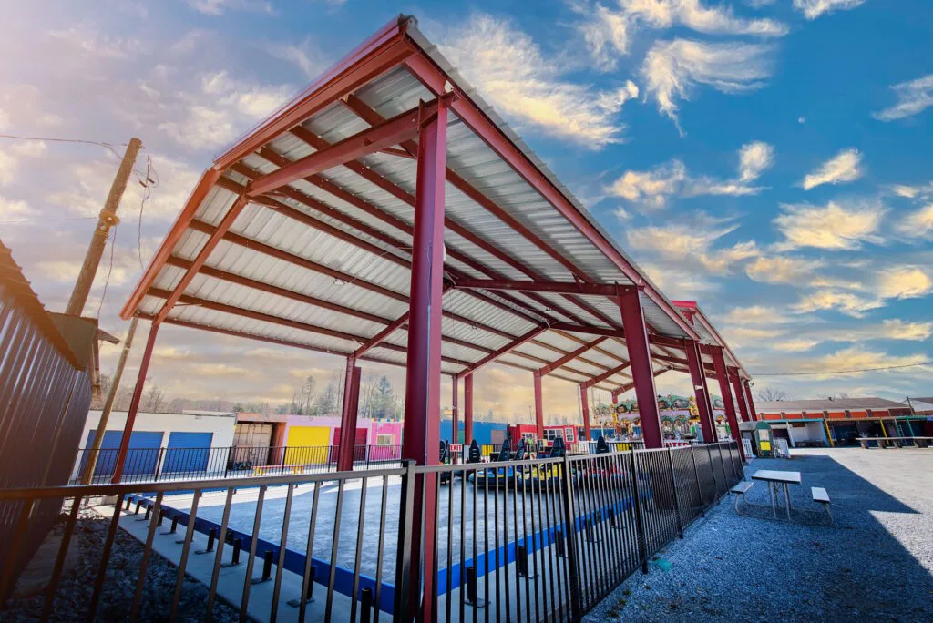 Red steel canopy structure with metal roofing over an outdoor commercial patio area in Buncombe County, NC.